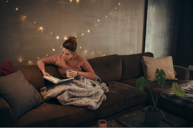 ソファーでマグカップ片手に読書する女性